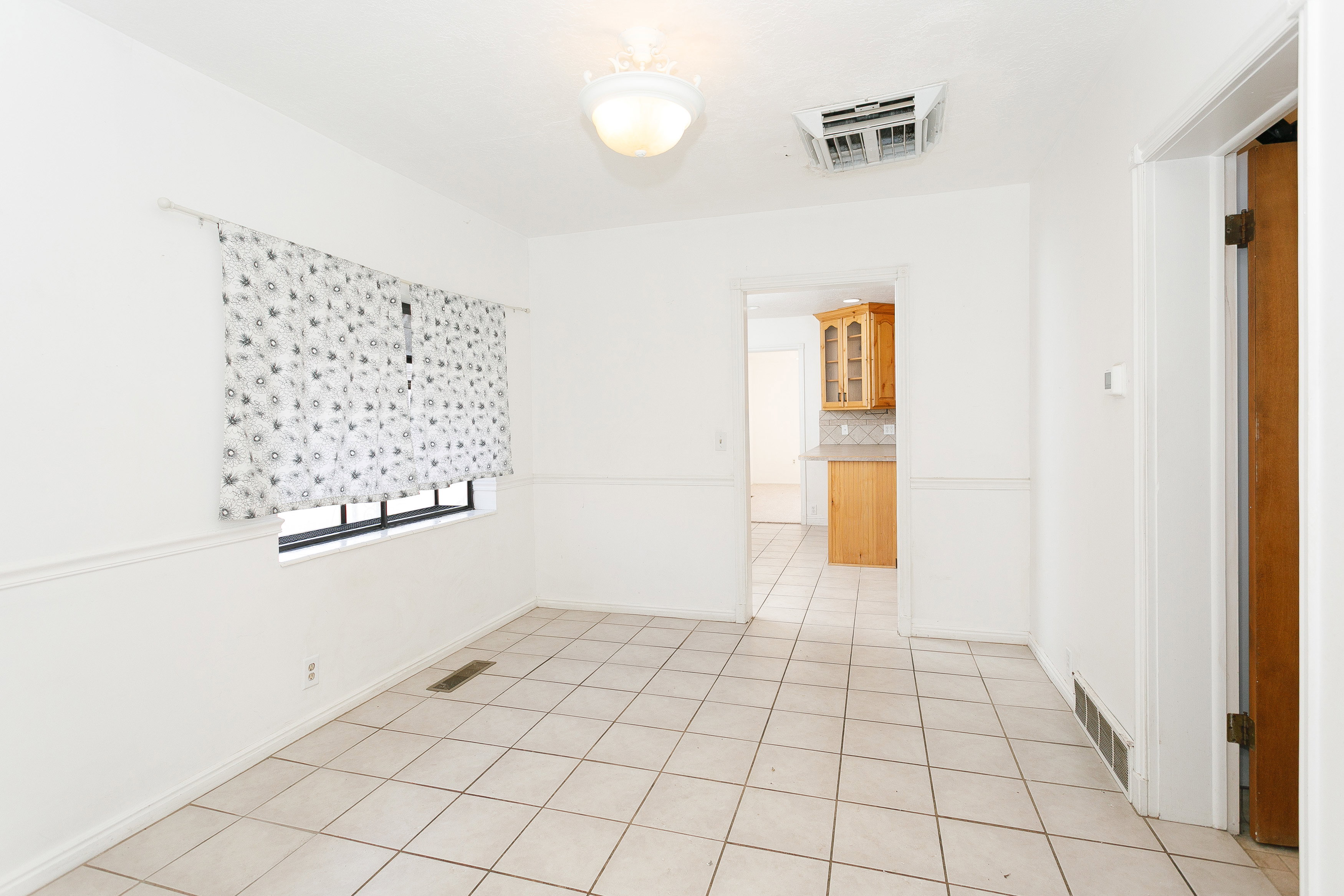 Bright interior space featuring light-toned tile flooring, white walls with wainscoting, and an overhead light fixture