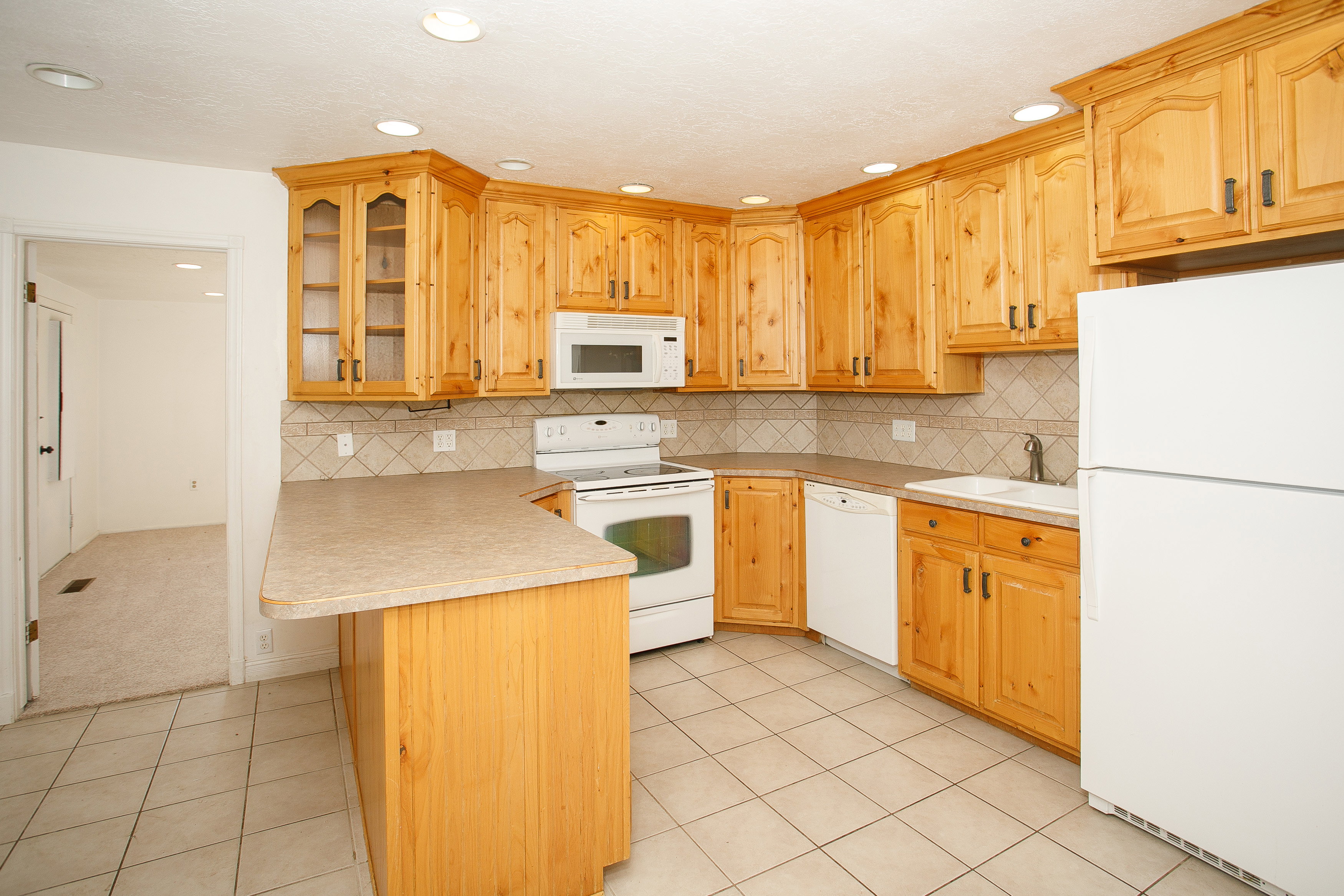 Kitchen featuring a U-shaped layout, wood cabinetry with glass-front accents, laminate countertops, tile flooring, and a tile backsplash