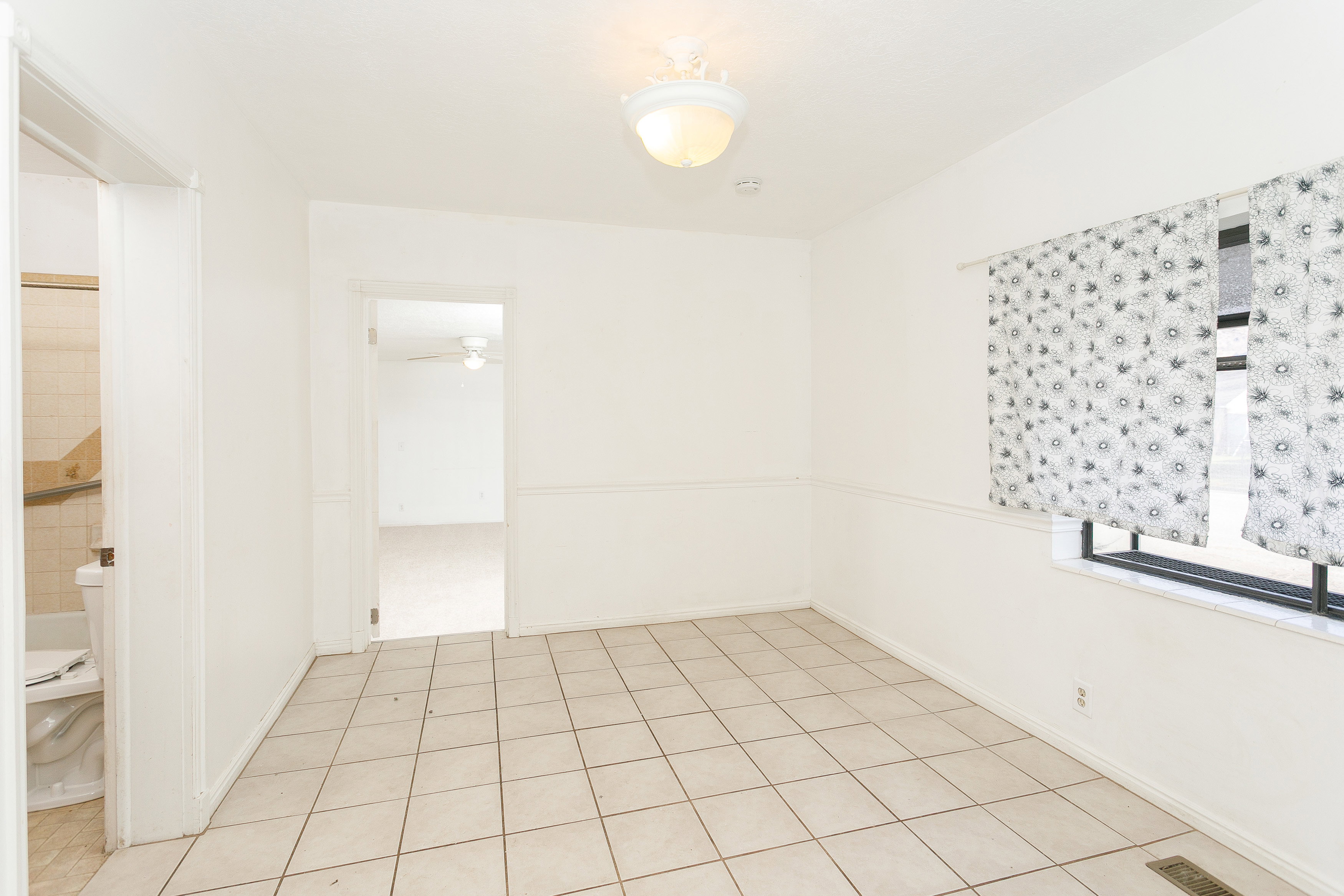 Neutral tone ceramic tile flooring, chair rail molding, and a prominent window with a deep sill