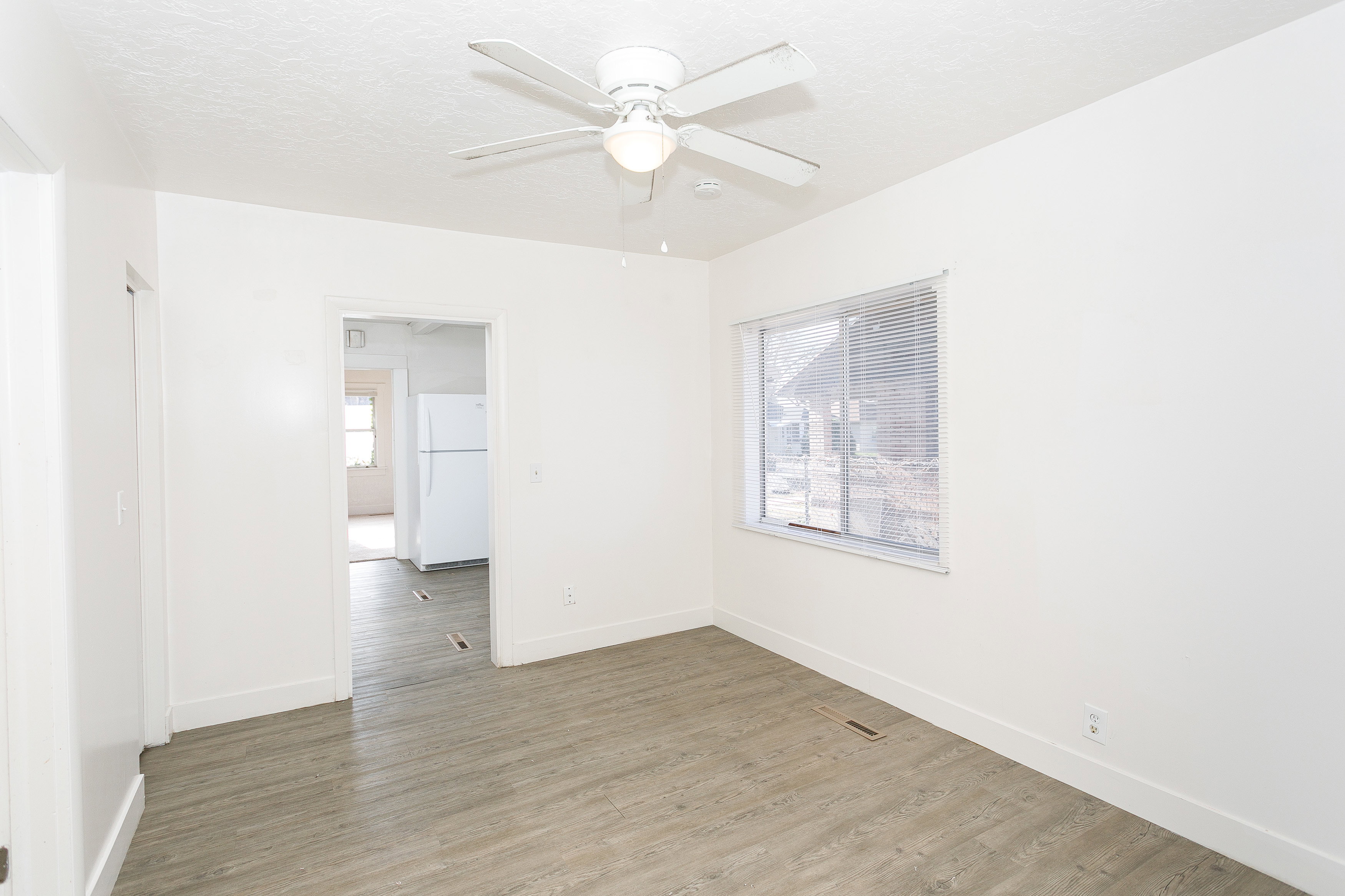 Room featuring wood-finish flooring, white walls, a ceiling fan with integrated lighting, and a window with blinds