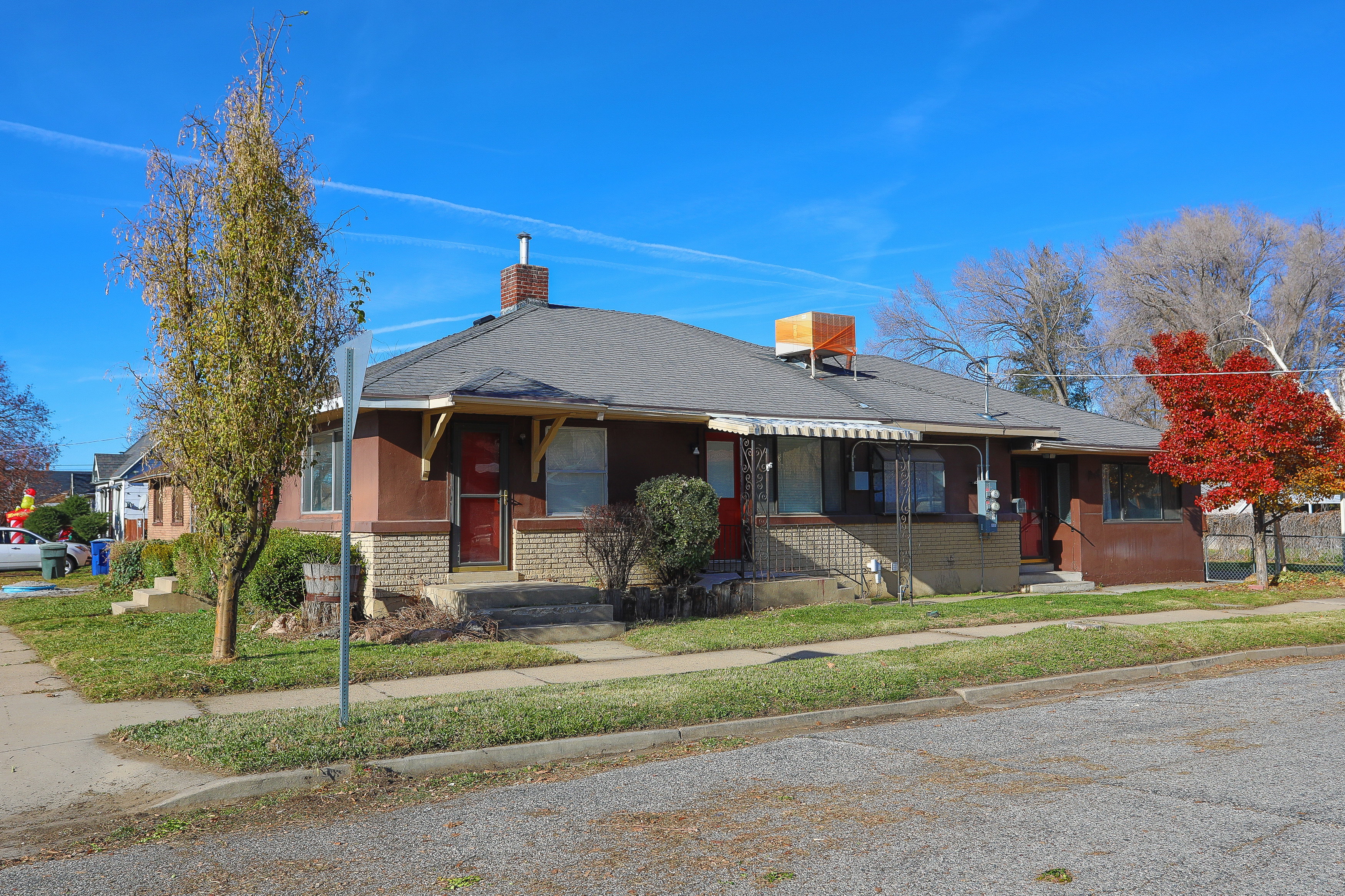 Residential structure featuring a brown stucco exterior, brick foundation, and a dark gray shingle roof