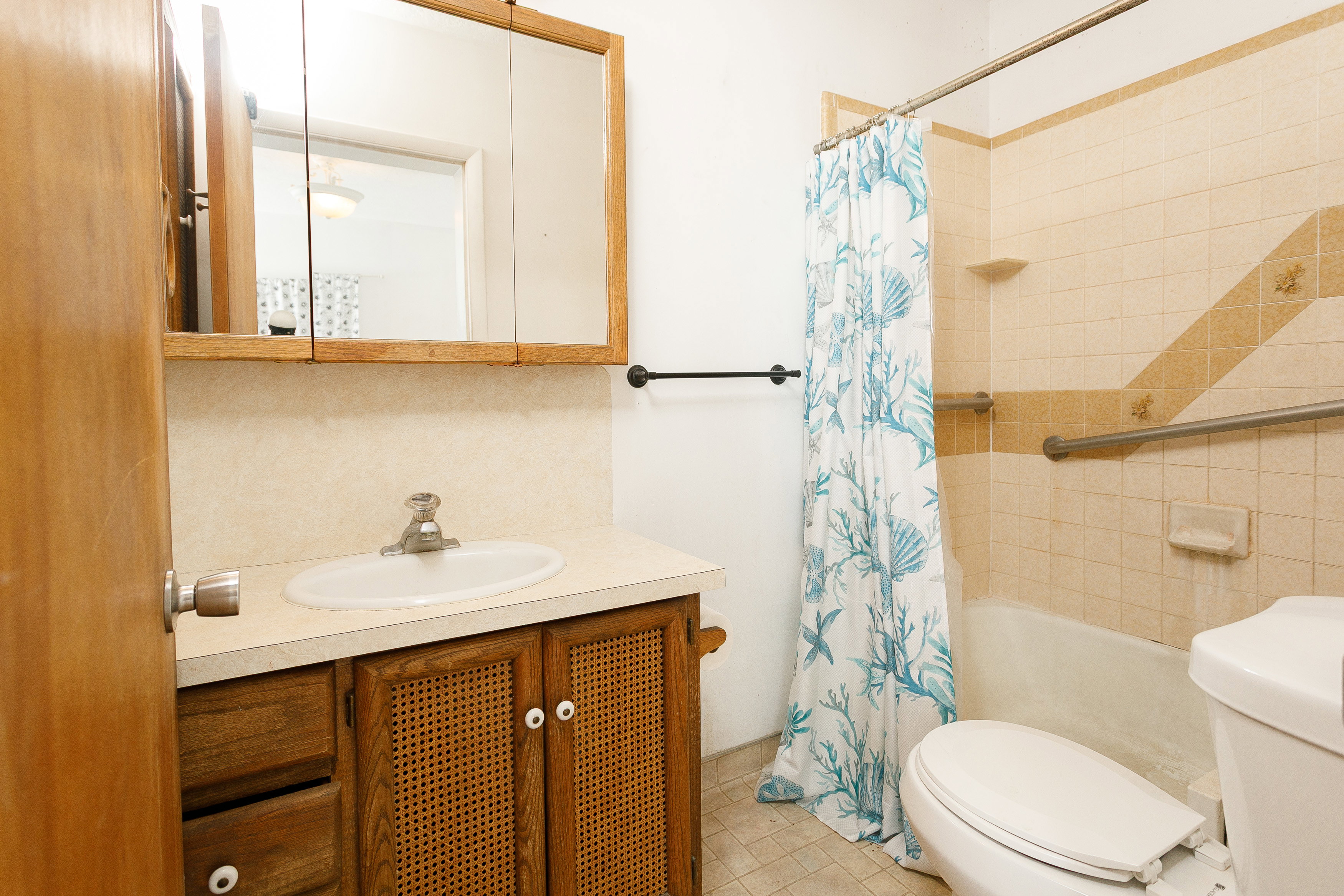 Bathroom featuring a wood-finish vanity with cane-style cabinet fronts, a white countertop, and an integrated white sink
