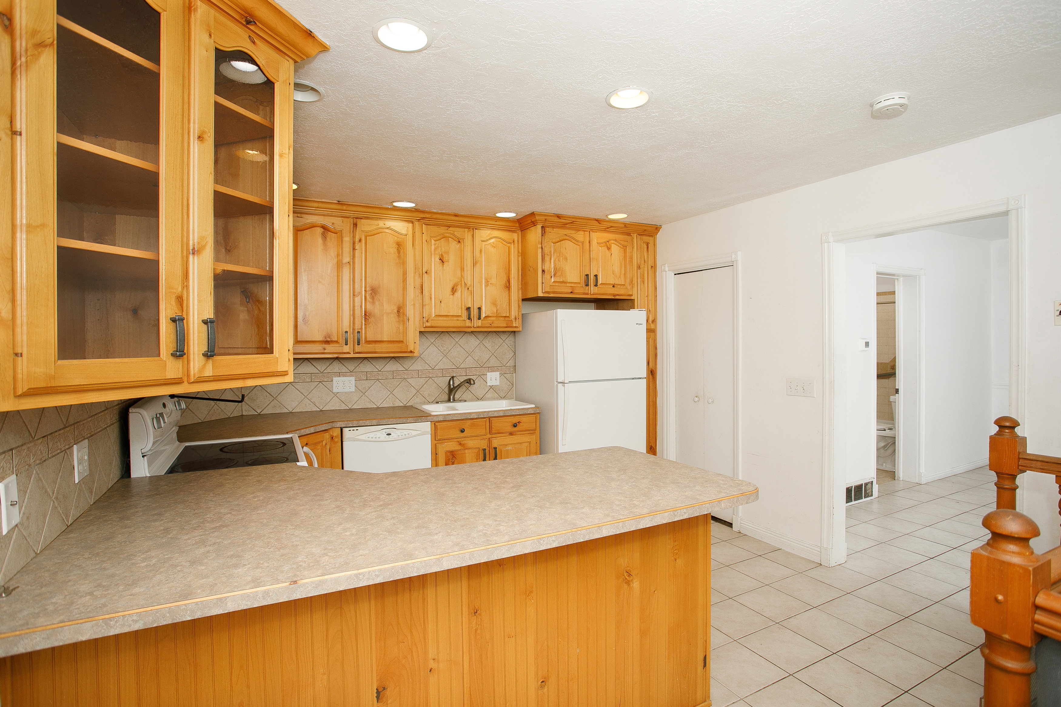 Kitchen featuring wood cabinetry with glass-front uppers, recessed lighting, and a neutral tile backsplash