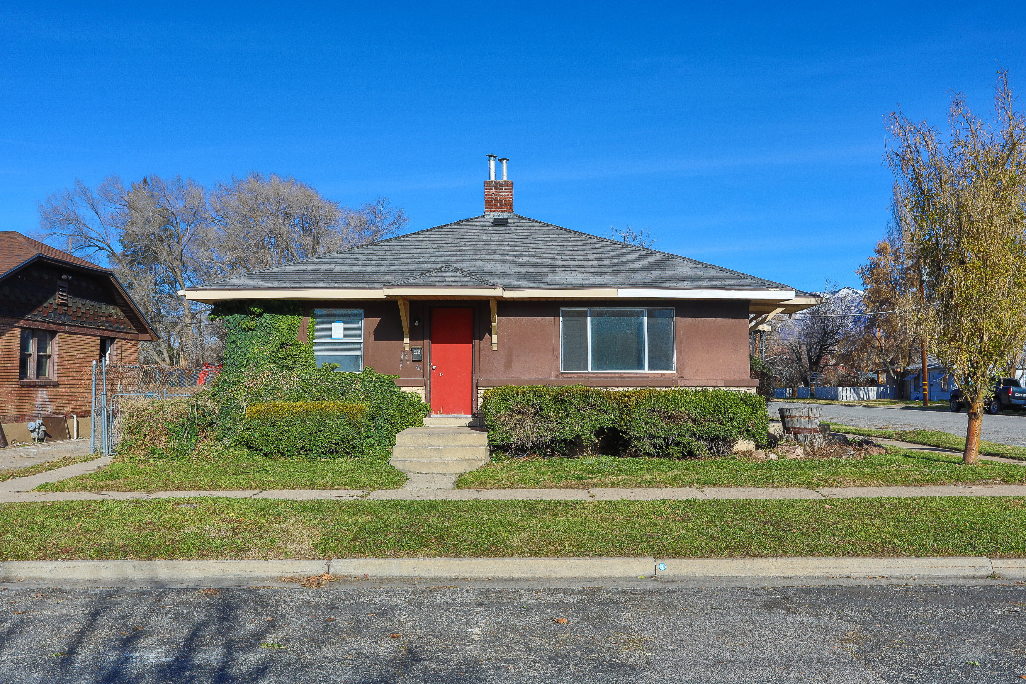 Single-story residence featuring a brown exterior, red entry door, and a dark gray shingle roof