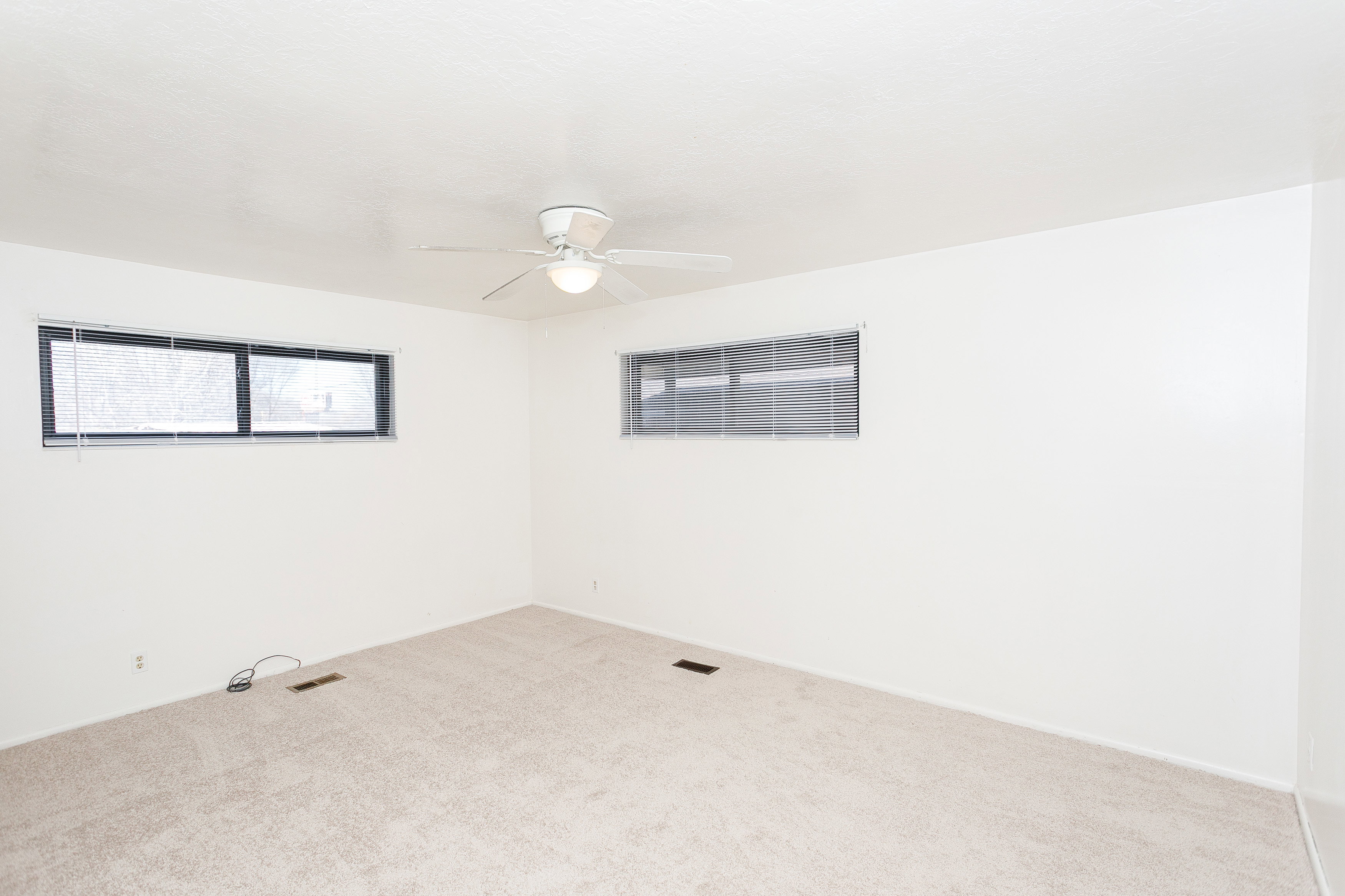 Carpeted room featuring multiple windows, a ceiling fan with integrated lighting, and white painted walls