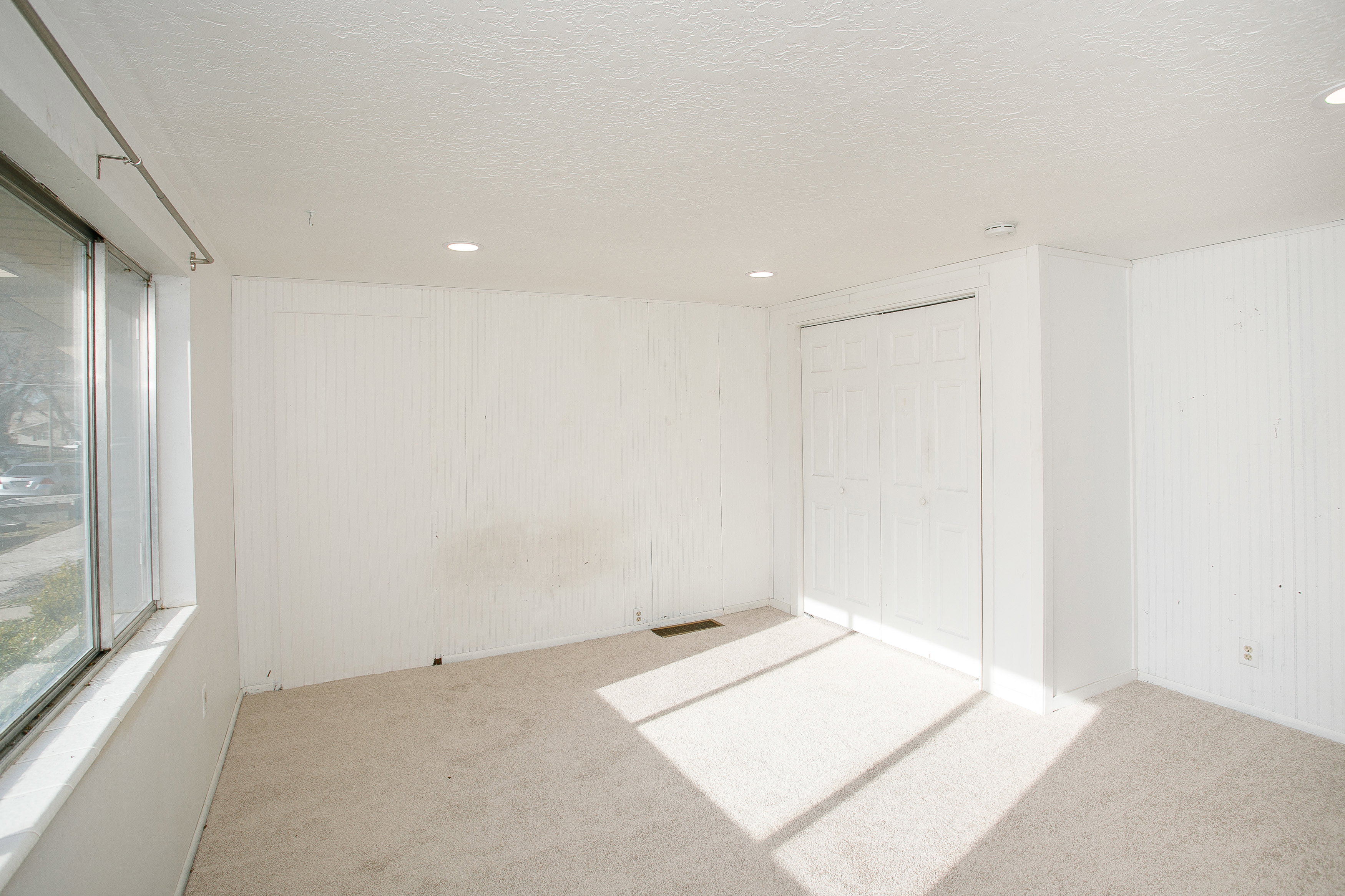 Room featuring light-colored carpeting, multiple recessed ceiling lights, and white beadboard wall paneling