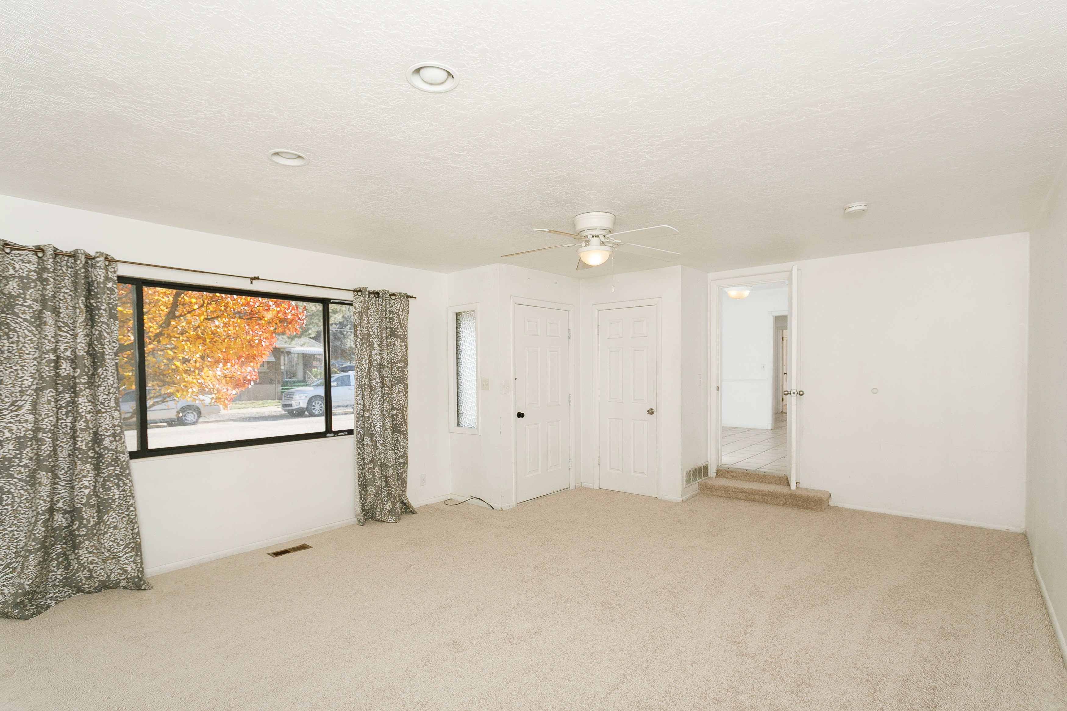 Carpeted interior space featuring a large window with black trim, recessed ceiling lighting, a ceiling fan, and white doors