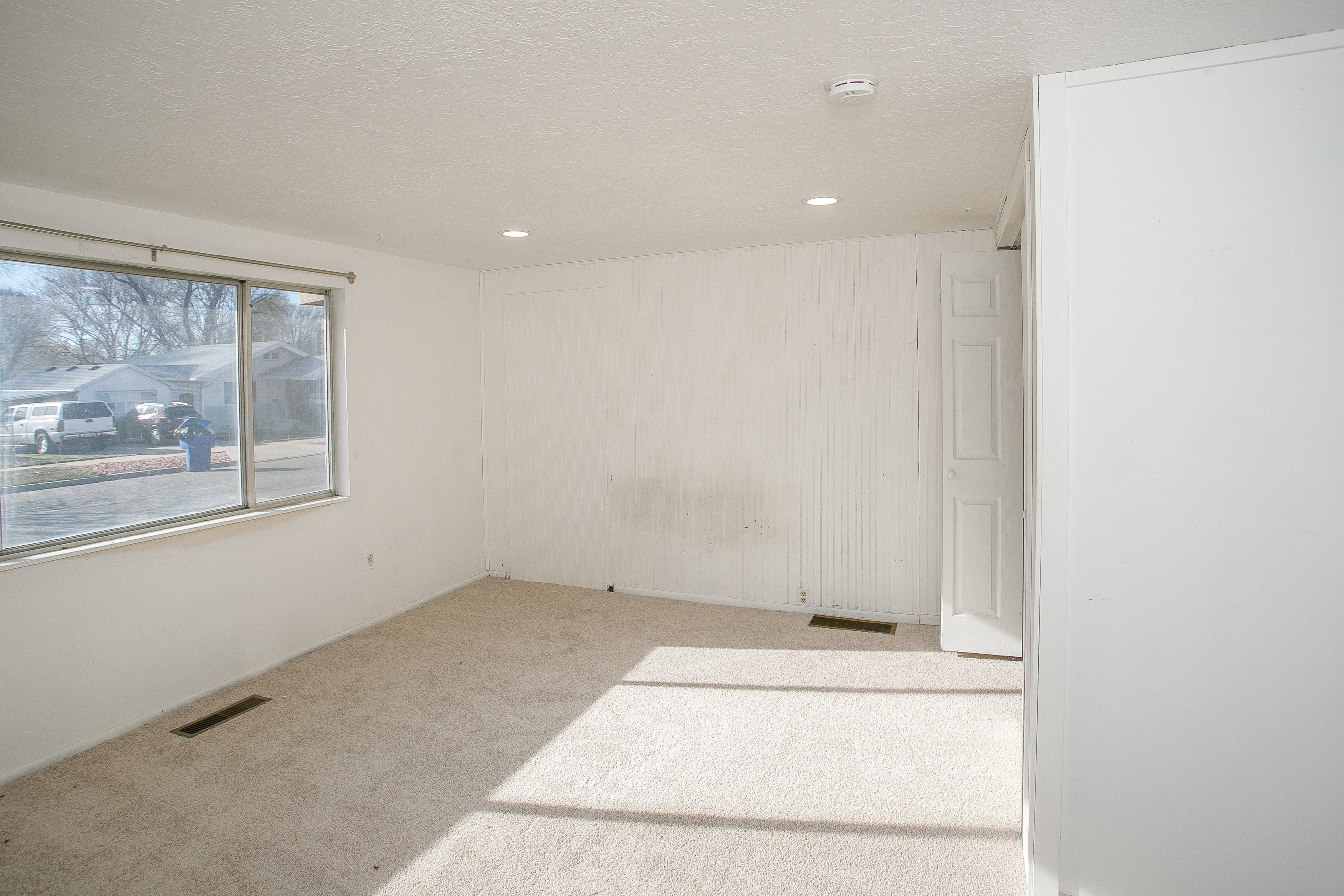 Bright interior space with a large window, recessed lighting, white paneled wall accents, and light-colored carpeting