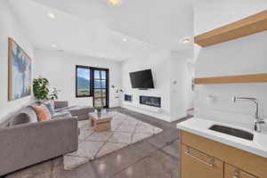 Open-concept living area featuring a modern fireplace, large black-framed window with mountain scenery, recessed lighting, and polished concrete flooring