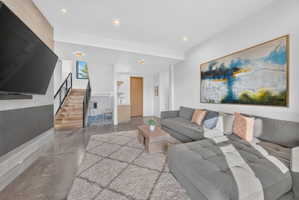 Spacious living area featuring polished concrete flooring and a modern staircase with wood treads and black metal railings