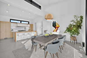 Open-concept living space featuring vaulted ceilings, recessed lighting, concrete flooring, and a contemporary kitchen with light wood cabinetry and an island