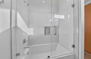 Bathtub with integrated shower, clear glass enclosure, chrome fixtures, white tile surround, and a recessed shower niche