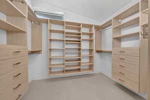 Custom closet system featuring light wood-finish cabinetry, extensive shelving, integrated drawers with dark hardware, and multiple hanging rods