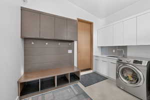 Laundry area featuring a built-in bench with cubby storage, wood-finish wall panels with hooks, and upper cabinetry