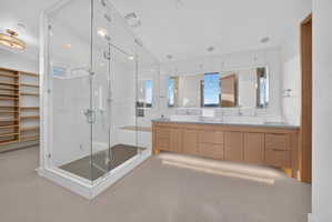 Modern bathroom featuring a frameless glass shower enclosure, a dual-sink vanity with wood-finish cabinetry, and a large built-in mirror
