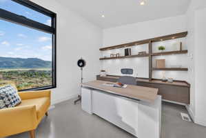 Dedicated workspace featuring a large picture window, custom built-in shelving with integrated lighting, recessed ceiling lights, and concrete-finish flooring