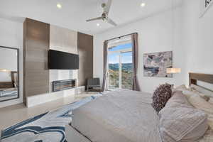 Bedroom with a modern linear fireplace set into a contrasting accent wall, featuring a ceiling fan, recessed lighting, and sliding glass doors opening to mountain terrain