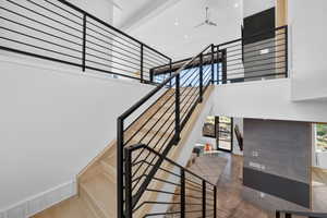 Contemporary open-concept interior featuring light wood-finish stairs with black metal railings, a double-height ceiling, and integrated ceiling fan