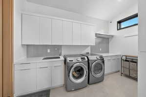 Spacious laundry area featuring extensive white cabinetry, light-toned countertops, a utility sink with a chrome faucet, and a large window providing ambient light