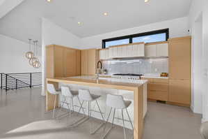 Open-concept kitchen featuring light wood-finish cabinetry, white subway tile backsplash, and an expansive island with a waterfall countertop