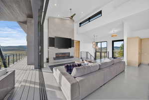Spacious living area featuring a vaulted ceiling with recessed lighting and clerestory windows, a stone-finish fireplace with an integrated linear firebox, and a wide sliding glass door opening onto a private deck with metal railings