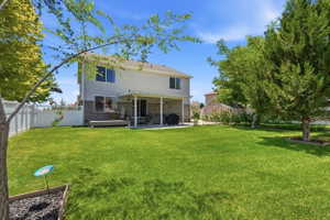 Spacious backyard featuring a large lawn, mature trees, white picket fencing, and a covered patio area