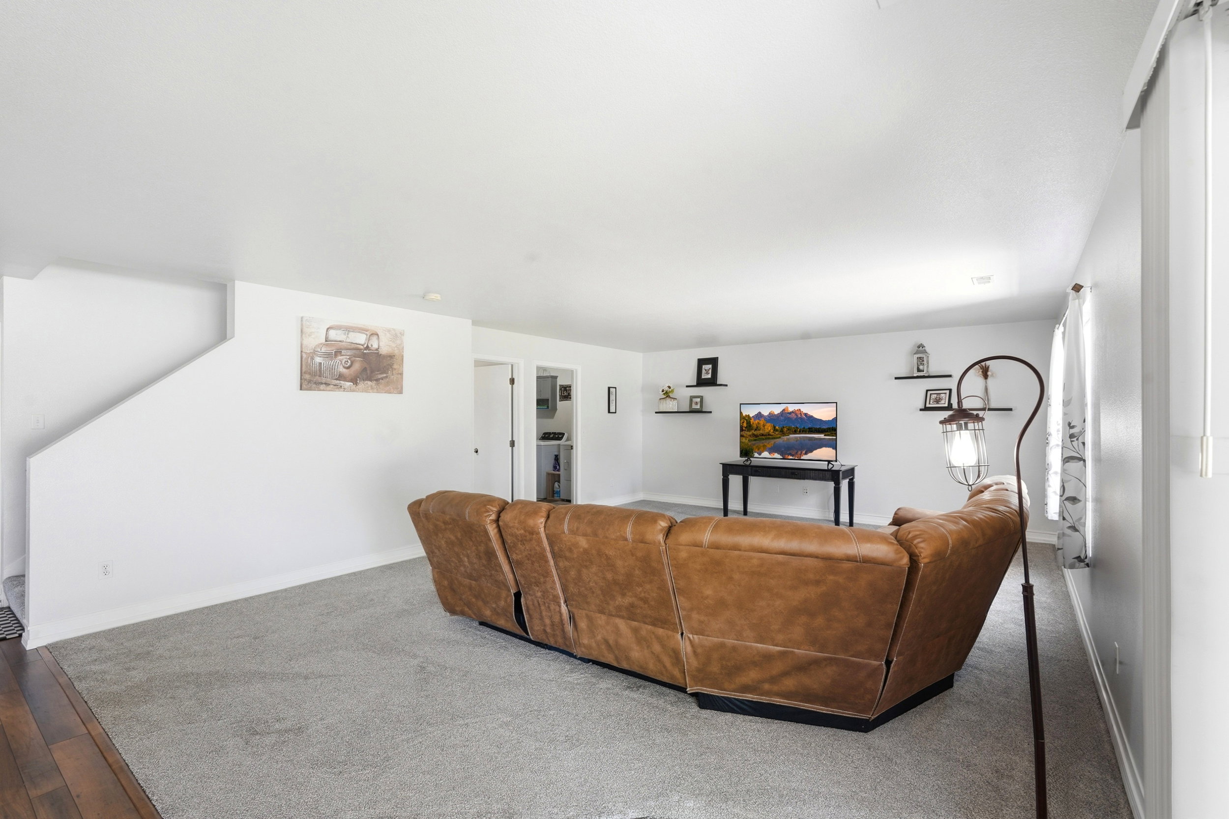 Open-concept living space featuring light gray walls, plush gray carpeting, built-in wall shelving, and a prominent window with vertical blinds