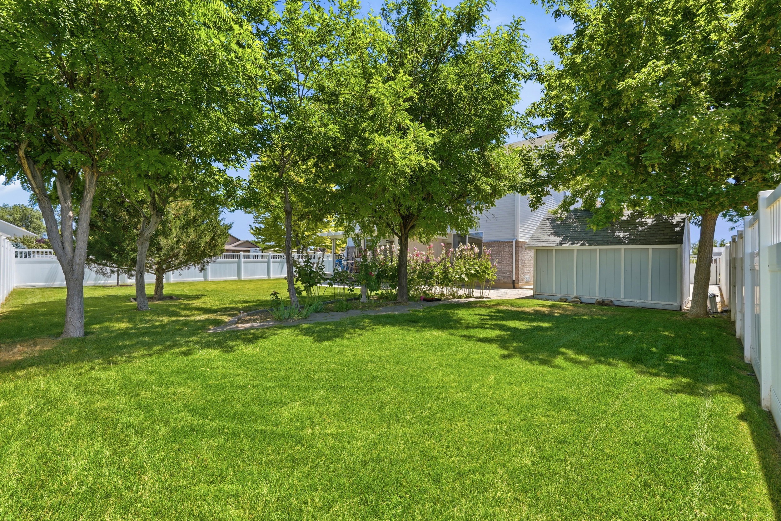 Expansive grassy yard with mature trees and a white privacy fence