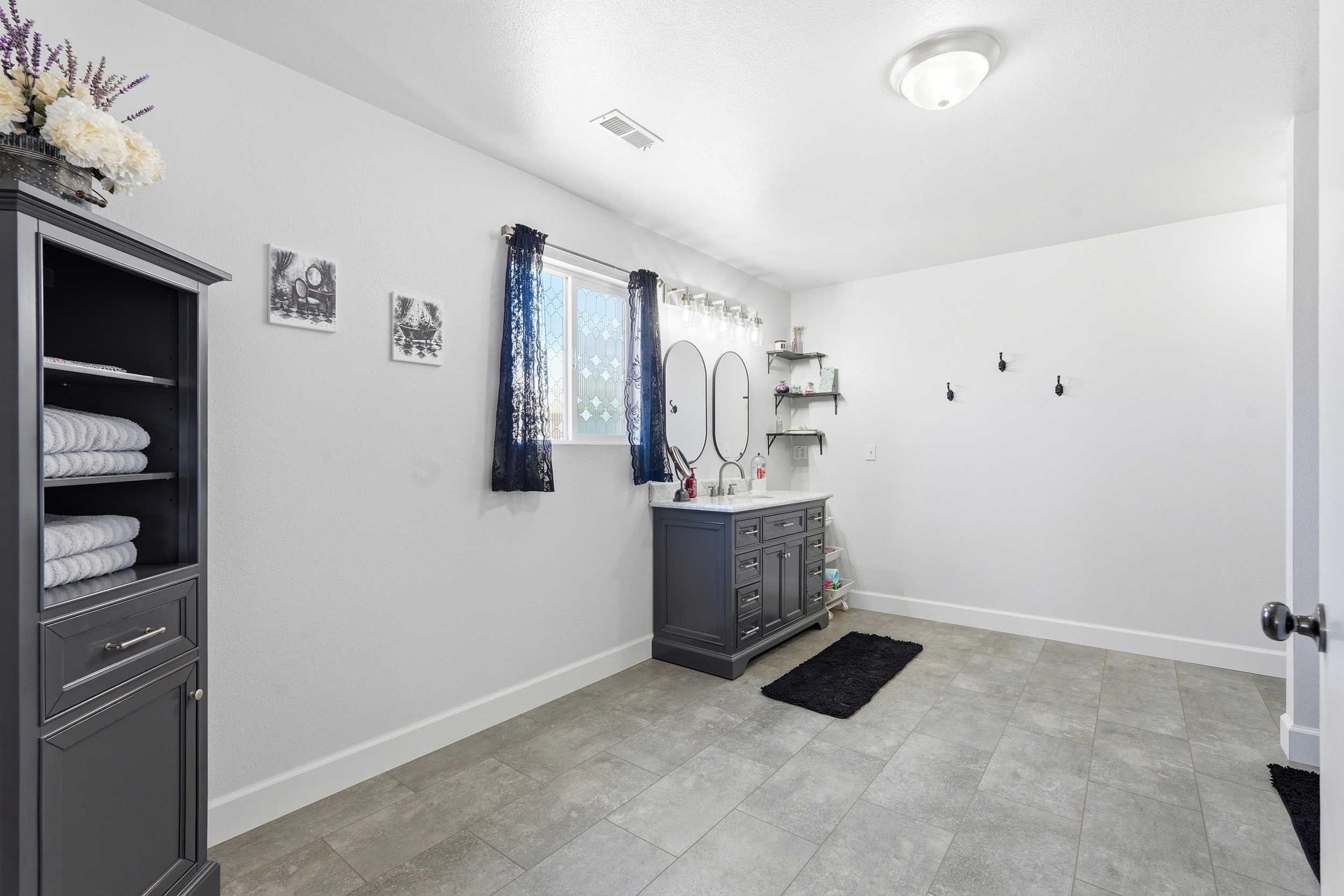 Spacious room featuring a dark grey vanity with dual sinks, overhead lighting, and built-in shelving