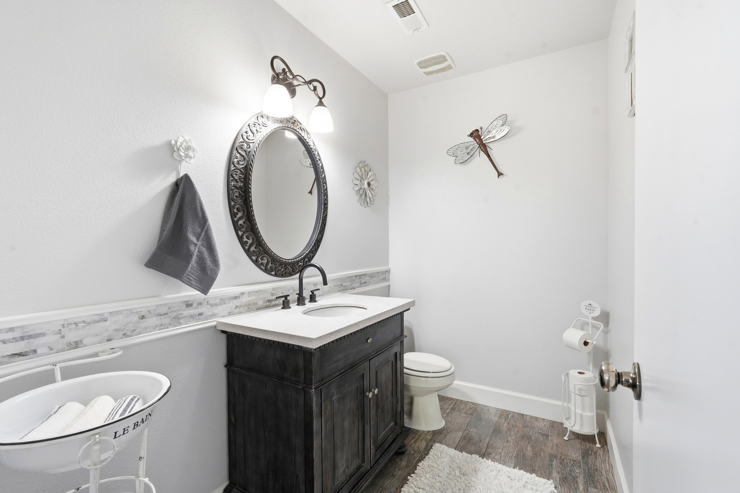 Bathroom featuring a dark wood vanity with a white countertop and oval sink, a decorative framed mirror, and a two-light vanity fixture