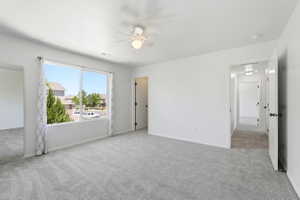 Spacious room featuring light gray carpet, white walls, a large window with a neighborhood perspective, and an overhead ceiling fan
