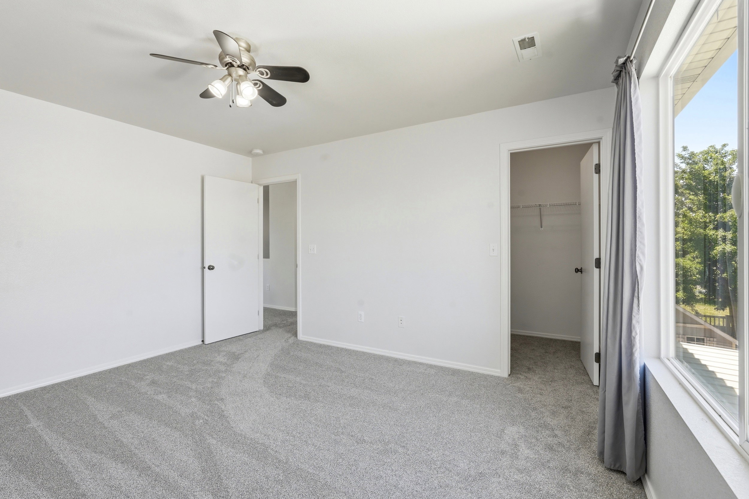 Carpeted interior room featuring a ceiling fan with integrated lighting, white walls, and a large window