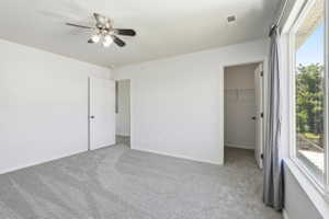 Carpeted interior room featuring a ceiling fan with integrated lighting, white walls, and a large window