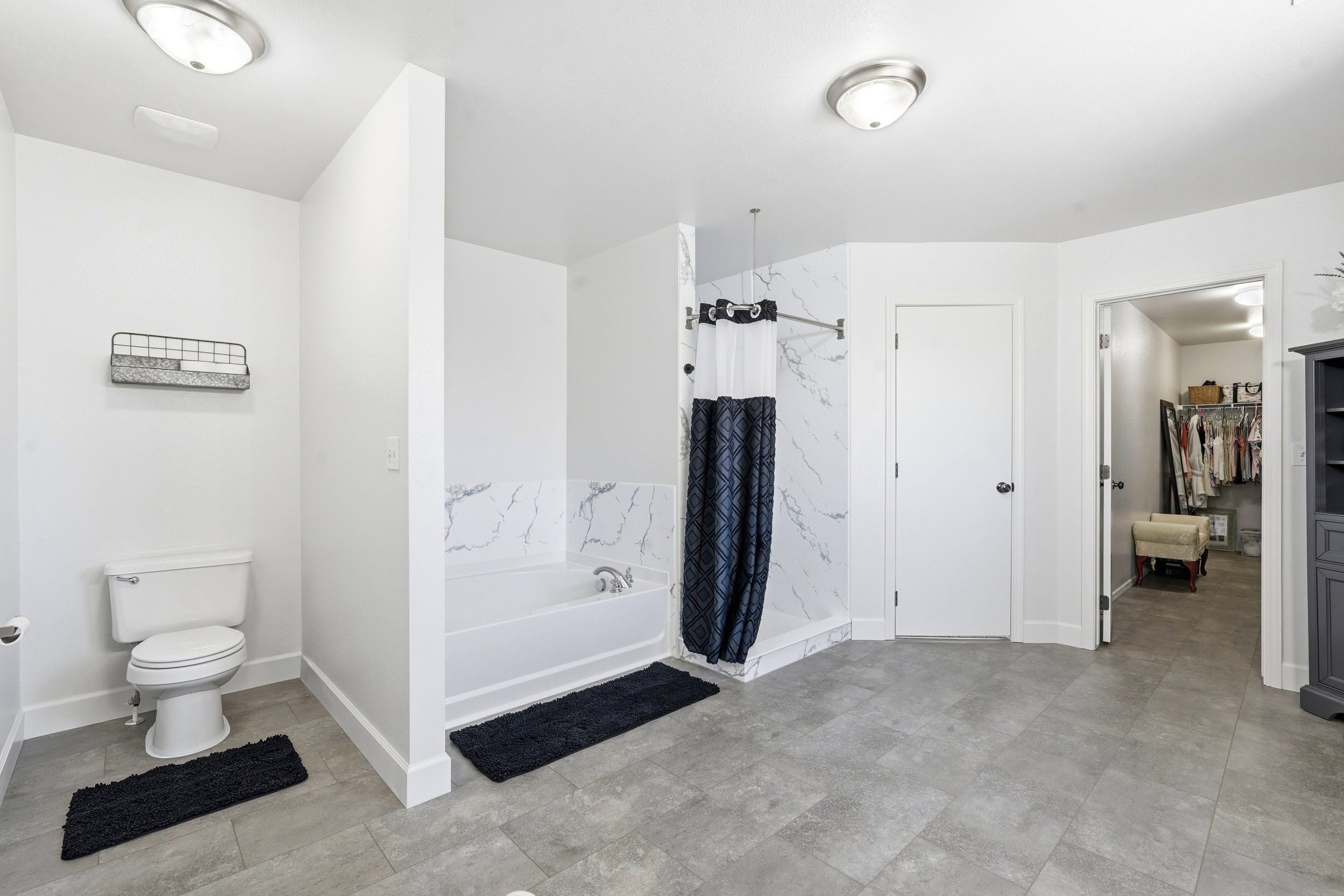 Bathroom featuring a white bathtub with a marble-patterned surround, a white toilet, and gray tile flooring