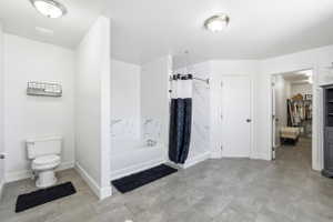 Bathroom featuring a white bathtub with a marble-patterned surround, a white toilet, and gray tile flooring