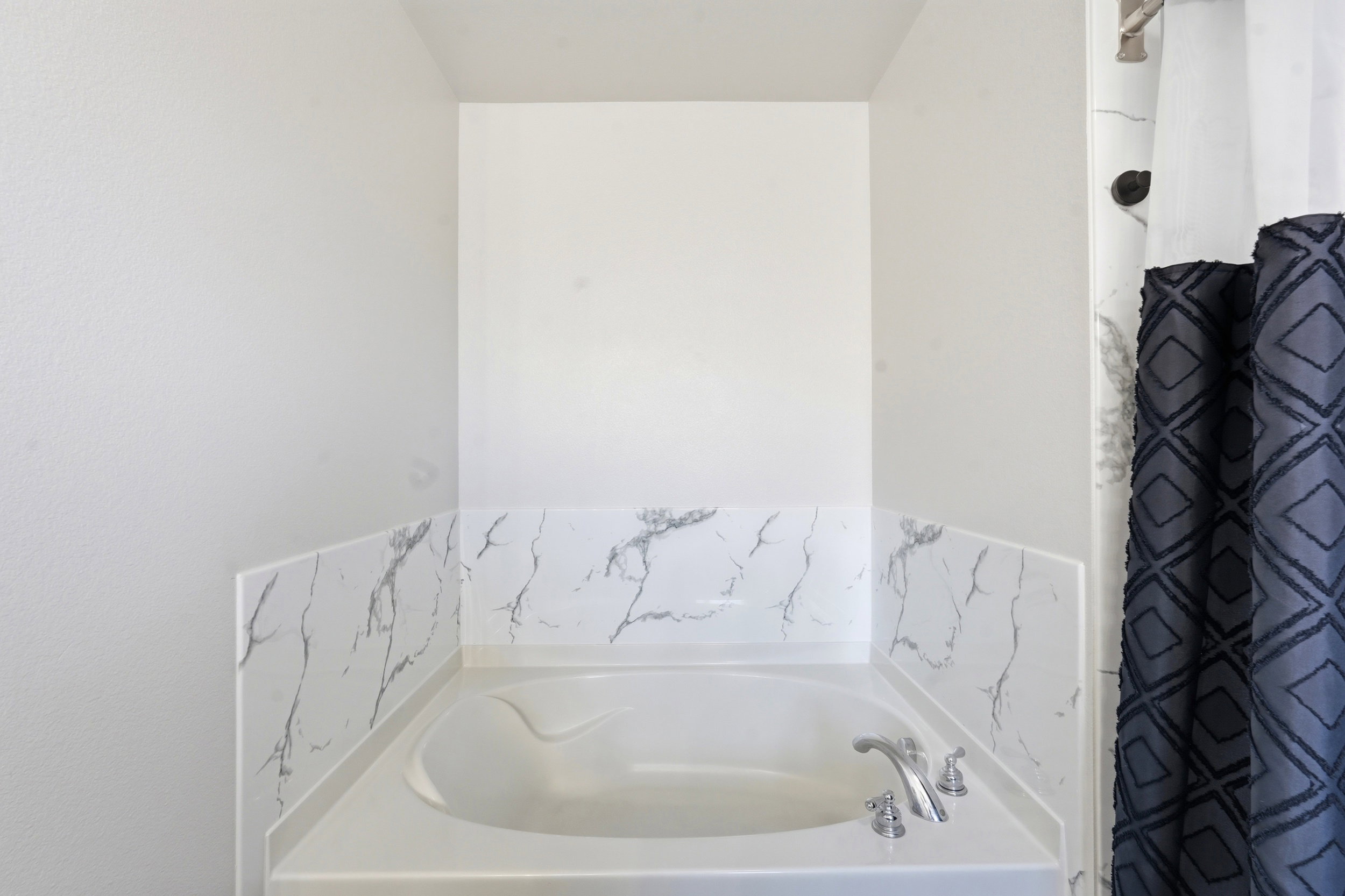 Built-in soaking tub with polished chrome fixtures and a white and gray marbled surround