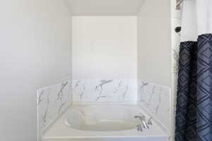 Built-in soaking tub with polished chrome fixtures and a white and gray marbled surround