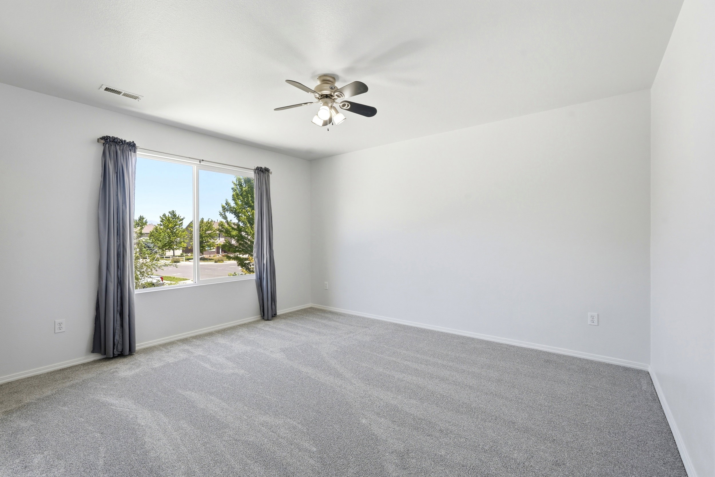 Bright room featuring a large window, plush gray carpeting, white walls, and a ceiling fan with integrated lighting