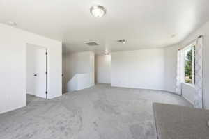 Spacious room featuring light gray carpet flooring, white walls, multiple flush-mount ceiling lights, a large window, and an open doorway