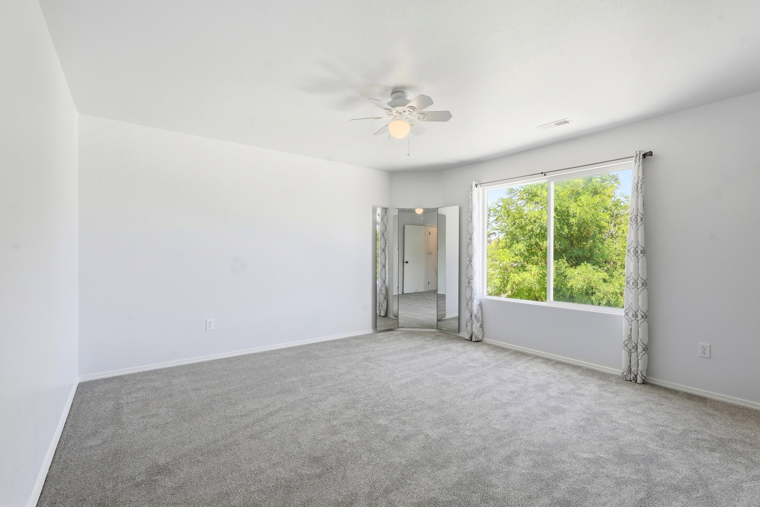 Spacious room featuring gray carpet, a ceiling fan with integrated lighting, and a large window showcasing exterior greenery