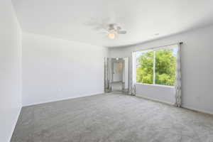 Spacious room featuring gray carpet, a ceiling fan with integrated lighting, and a large window showcasing exterior greenery