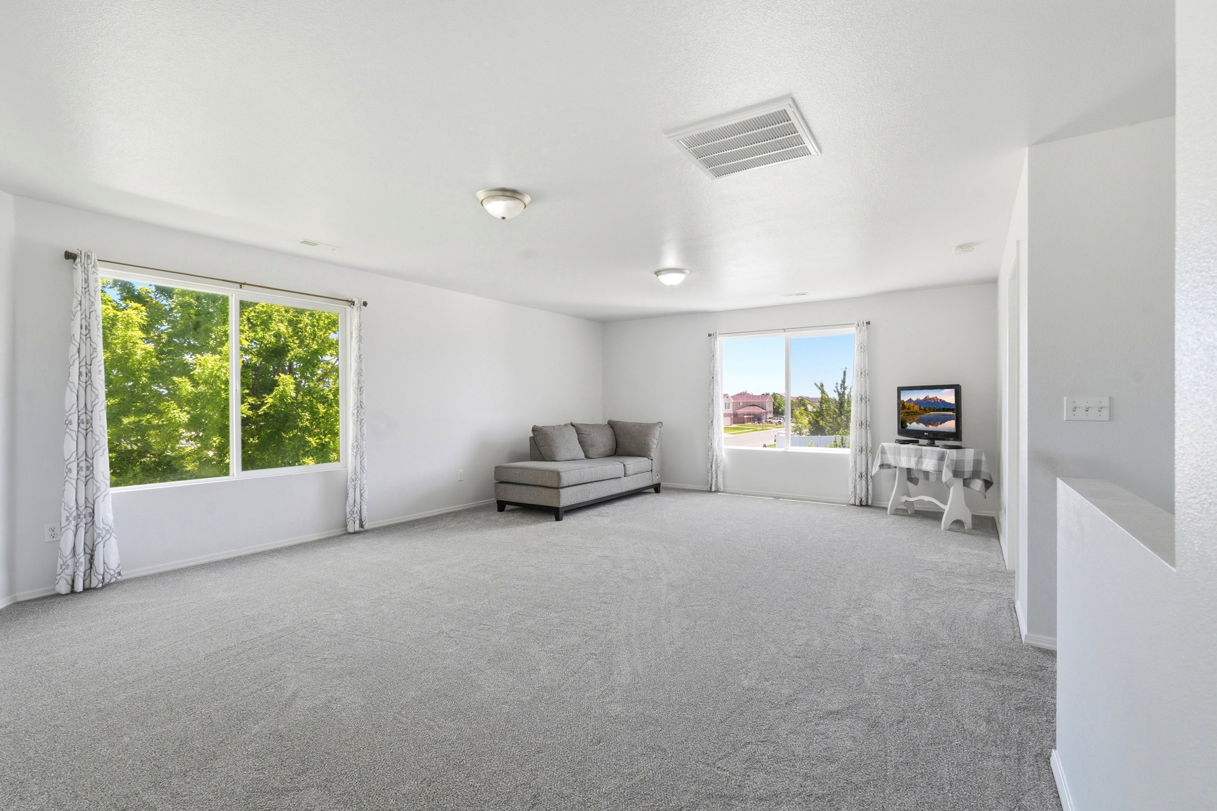 Spacious interior room featuring light gray carpeting, multiple large windows, and a neutral wall palette