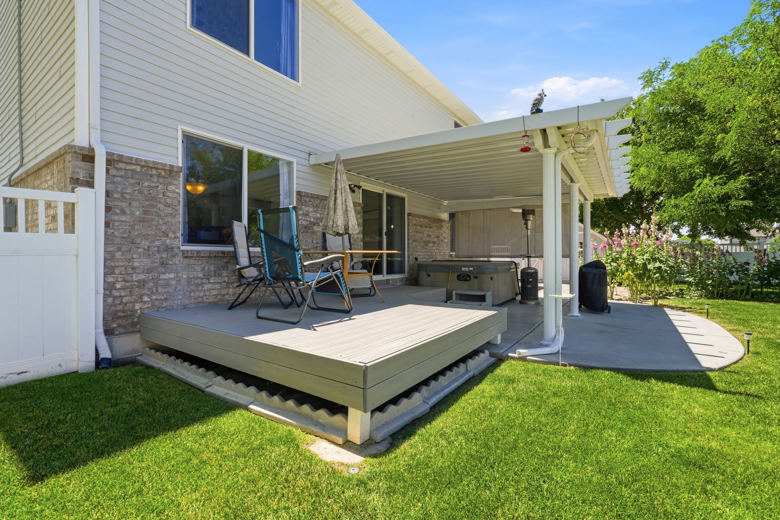 Expansive backyard featuring a covered patio with a hot tub, an elevated composite deck, and a manicured lawn