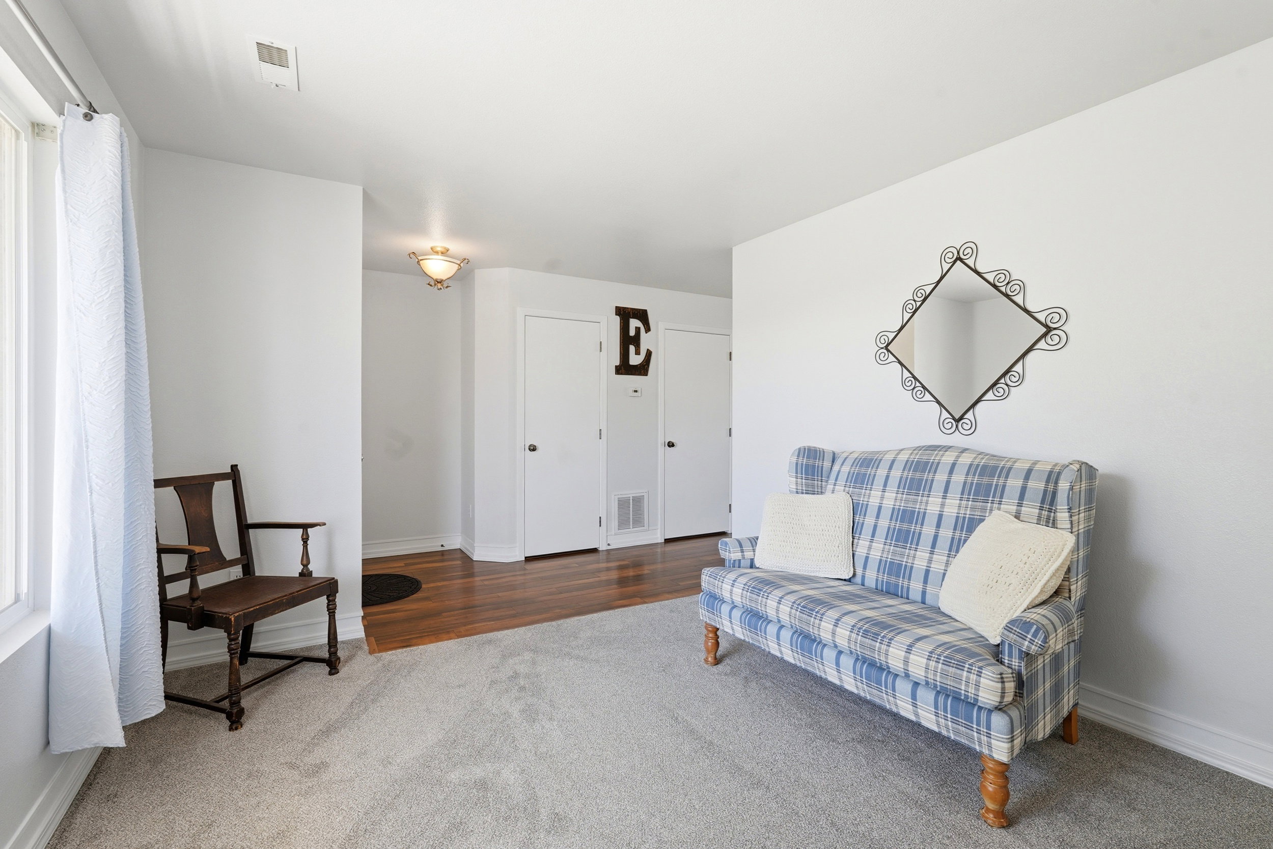 Bright interior space featuring light gray carpeting, white painted walls, a large window, a ceiling vent, and a flush-mount light fixture