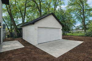 Detached garage with white siding, a black shingled roof, and a panel garage door