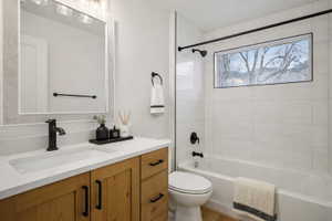 Bathroom featuring a wood-finish vanity with a built-in sink, a rectangular mirror with a textured frame, and a bathtub with white tile surround