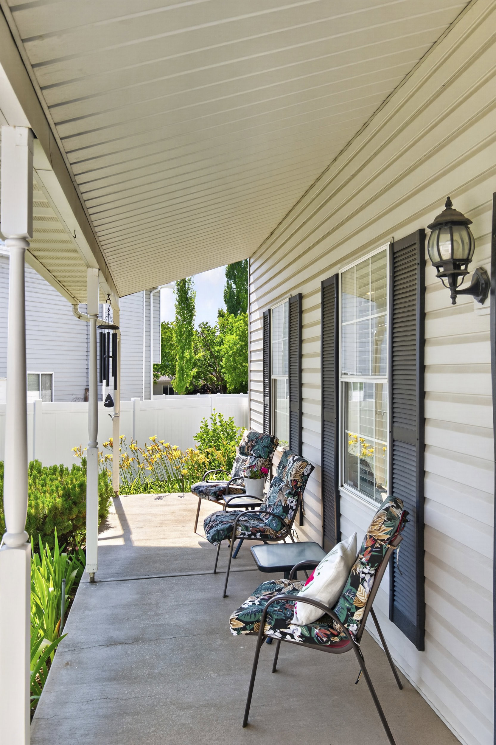 Covered concrete porch featuring a white vinyl siding exterior, a white picket fence, and dark window shutters