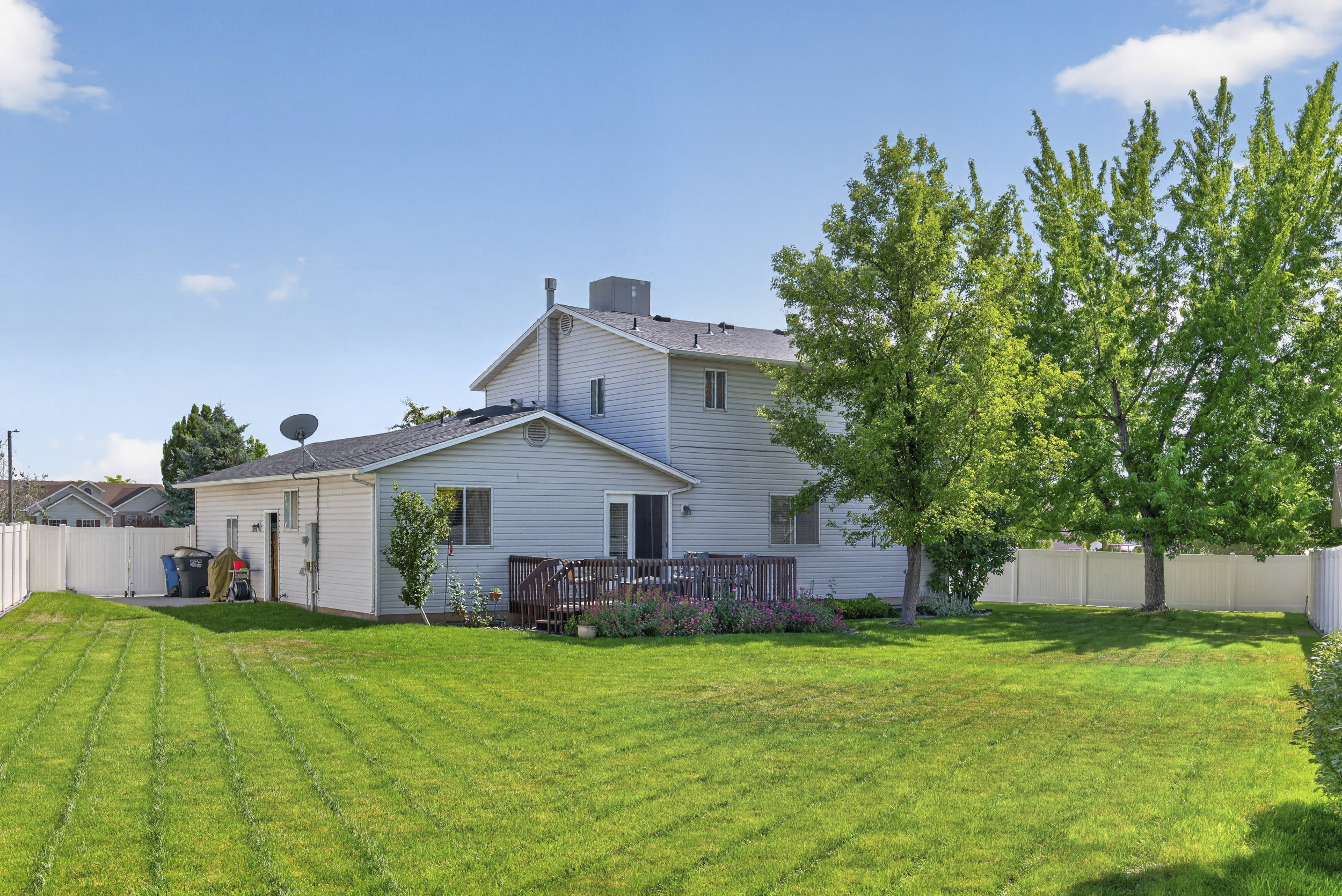 Expansive, fenced backyard featuring a manicured lawn, mature trees, and a multi-level wood deck with plantings