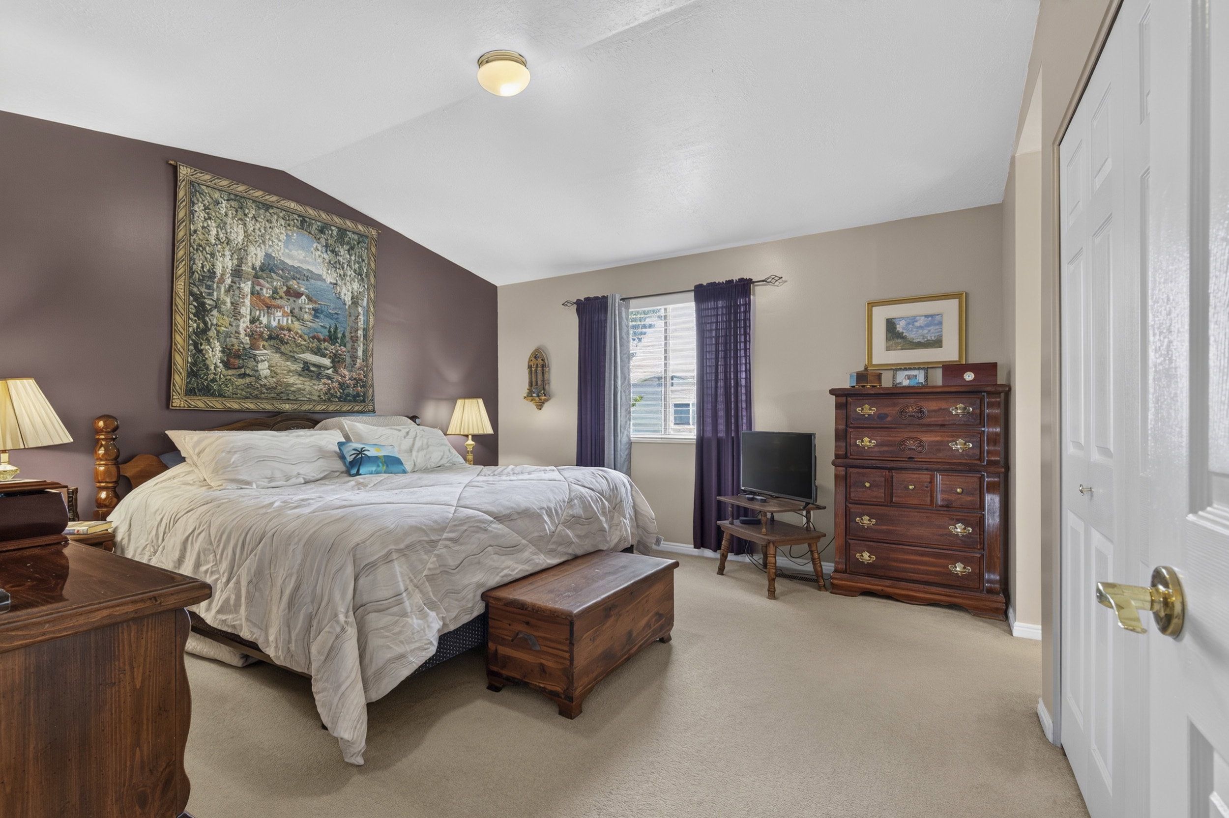 Expansive room featuring a window with white blinds and deep purple drapes, a vaulted ceiling, and carpet flooring