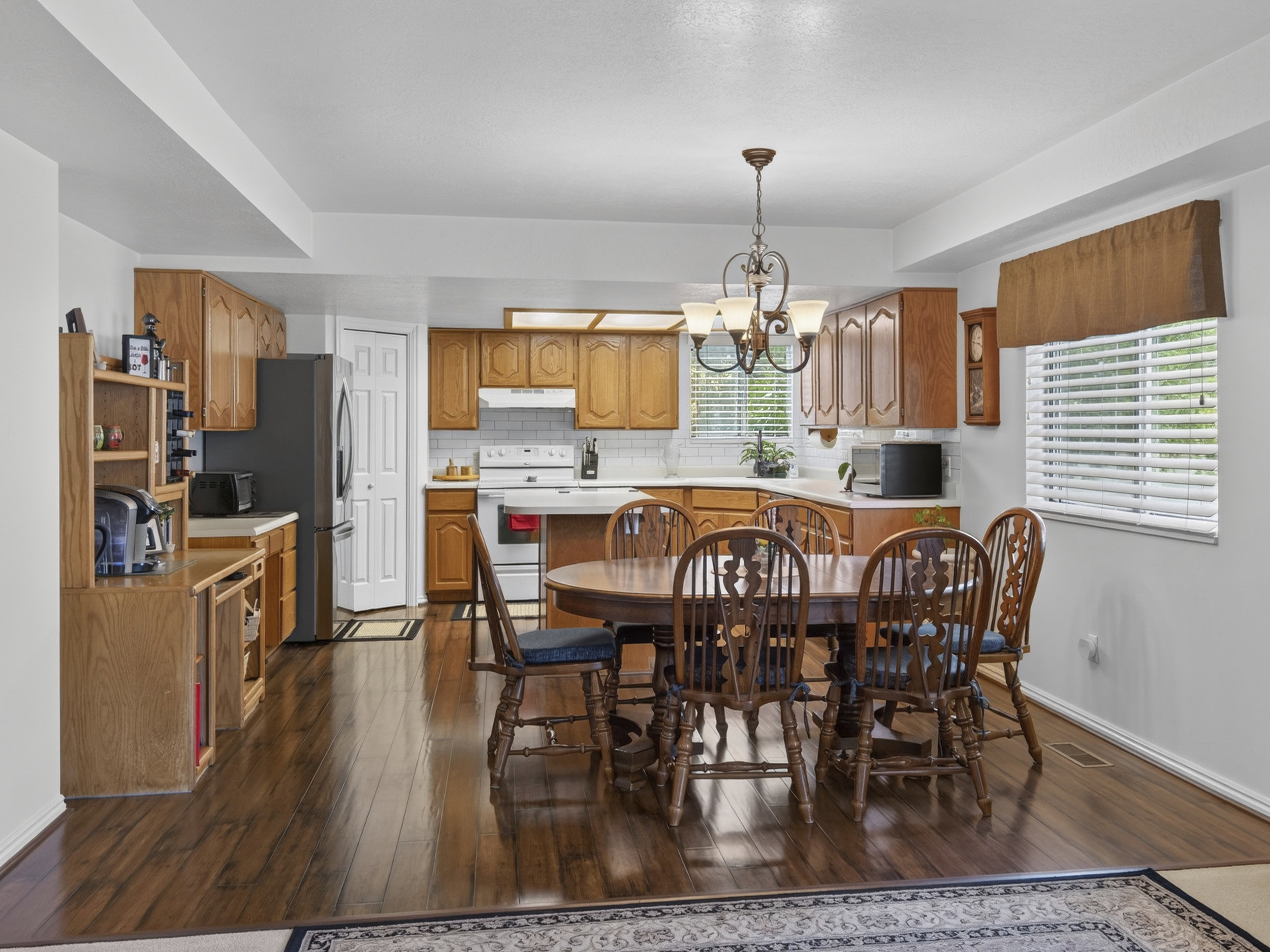 Open-concept kitchen and dining area featuring wood-finish flooring, oak cabinetry, white subway tile backsplash, and a decorative chandelier